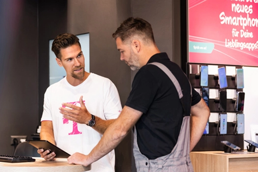 Verkäufer berät Kunden im Smartphone-Shop, Tablet und Handy-Auswahl am Tresen