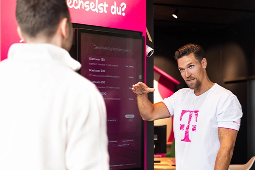 Telekom Mitarbeiter erklärt Glasfaser-Tarife am Display im Shop